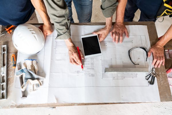 Construction Workers Collaborating on Site Plan Overhead view of construction workers discussing blueprints with digital tablet and tools on table.